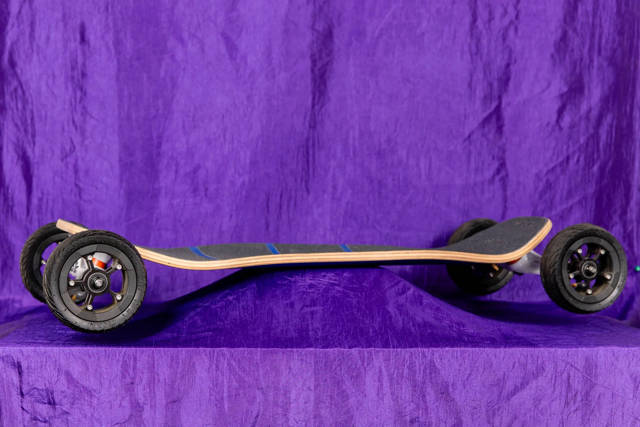 Off-road skateboard with large wheels, purple background.