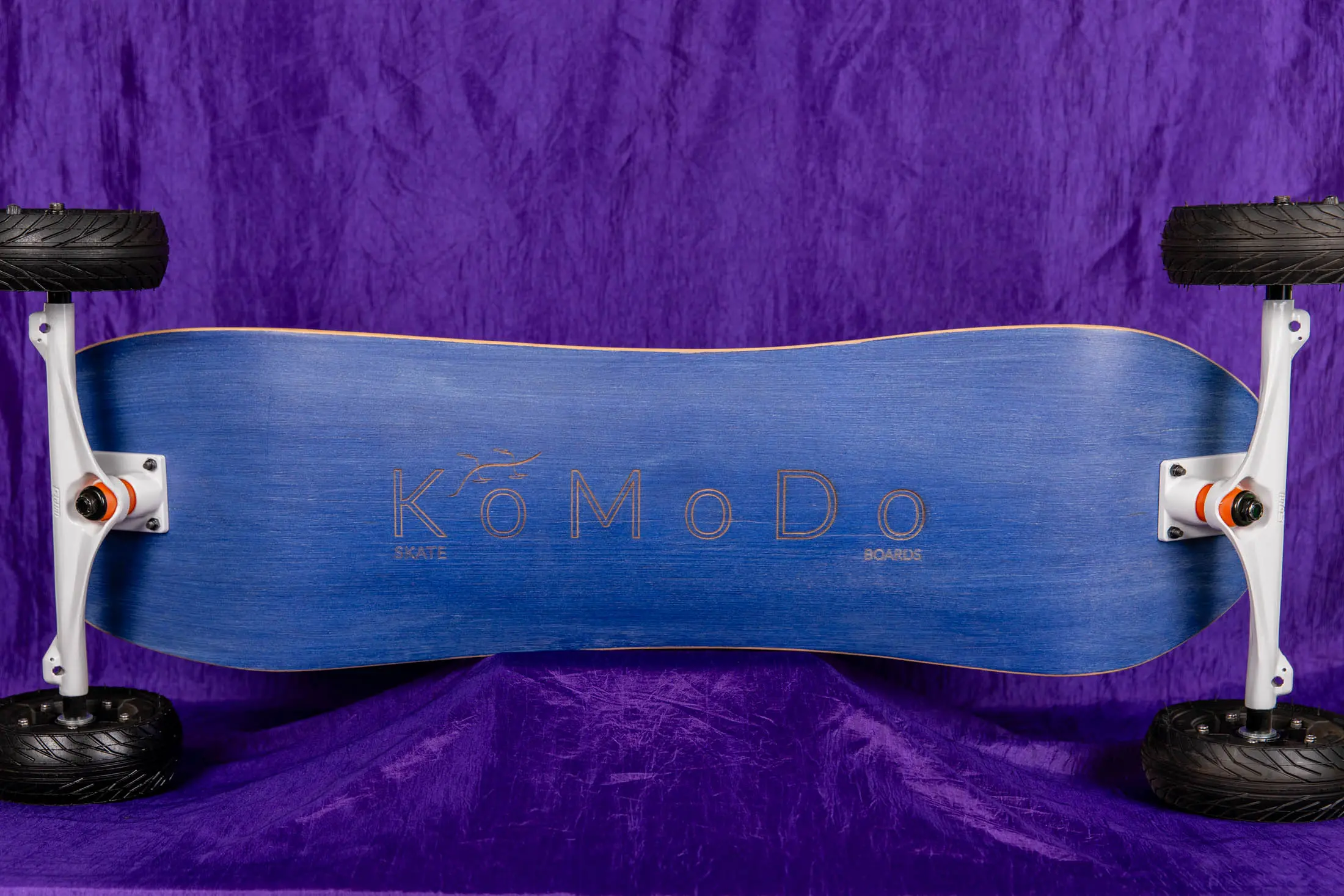Blue skateboard with large wheels, purple background.