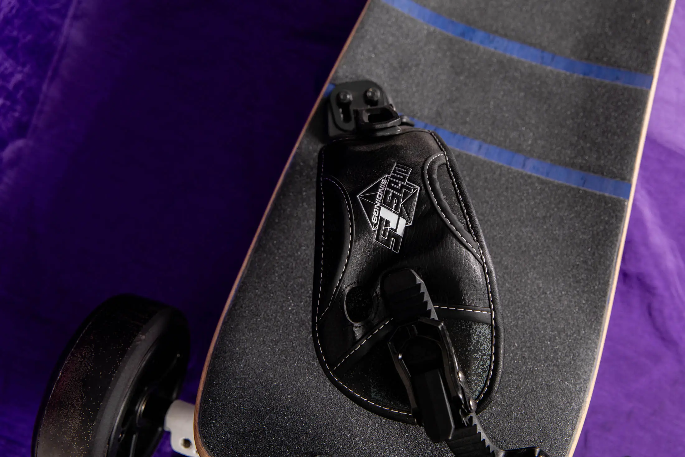 Electric skateboard with foot strap, purple background.
