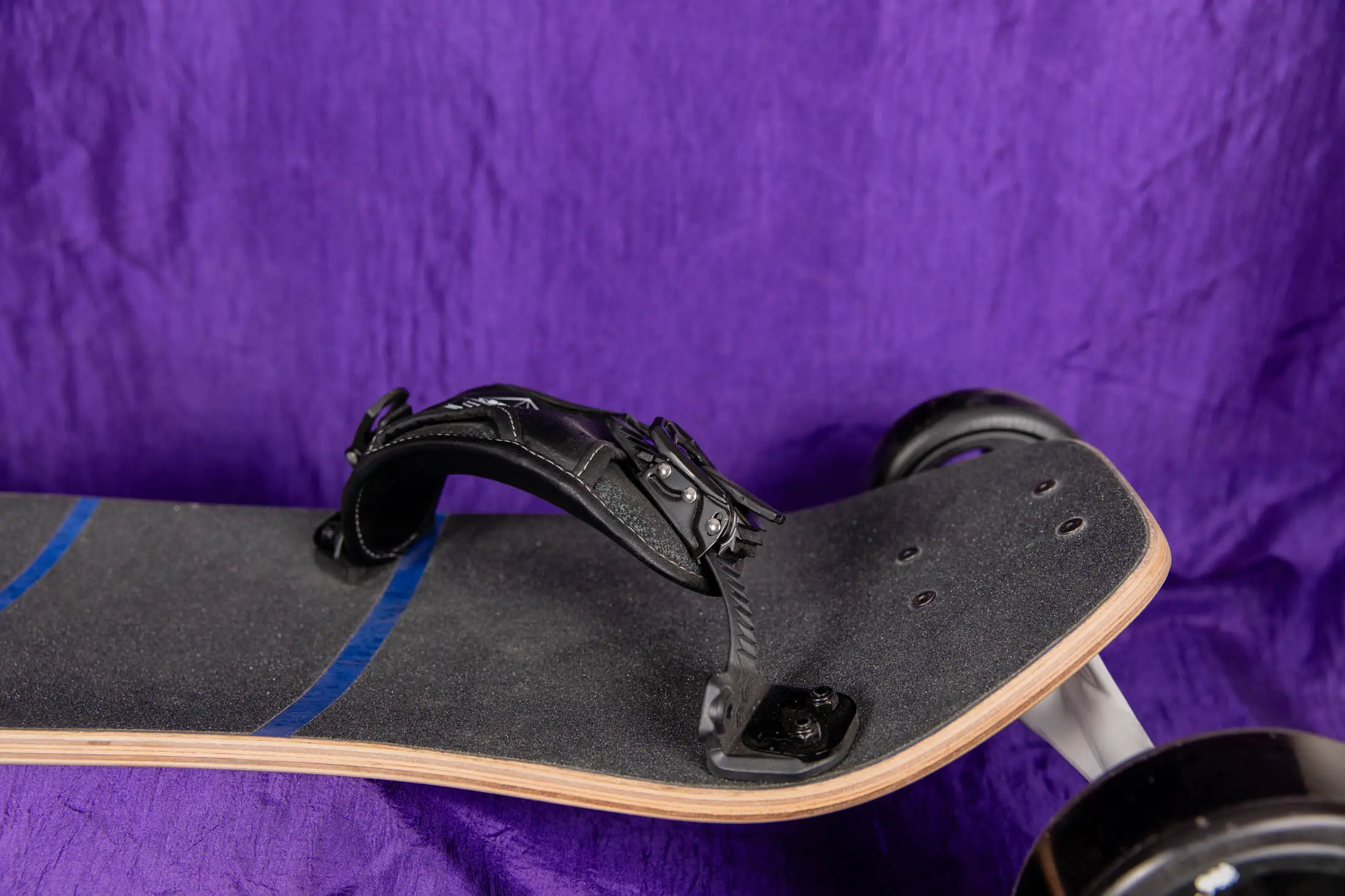 Electric skateboard with foot strap, purple background.
