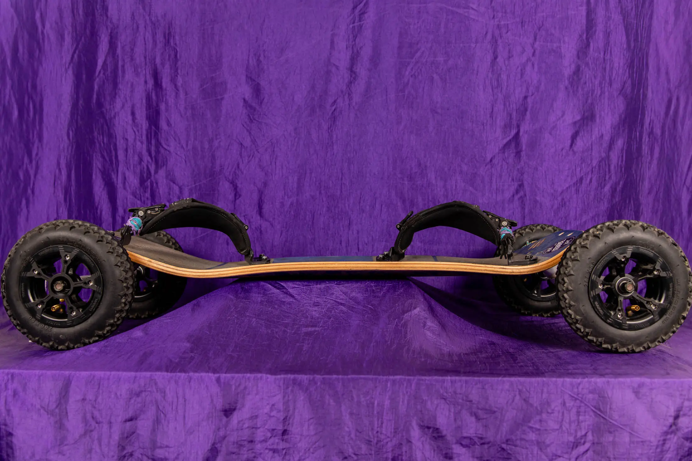 Off-road skateboard with large wheels, purple background.