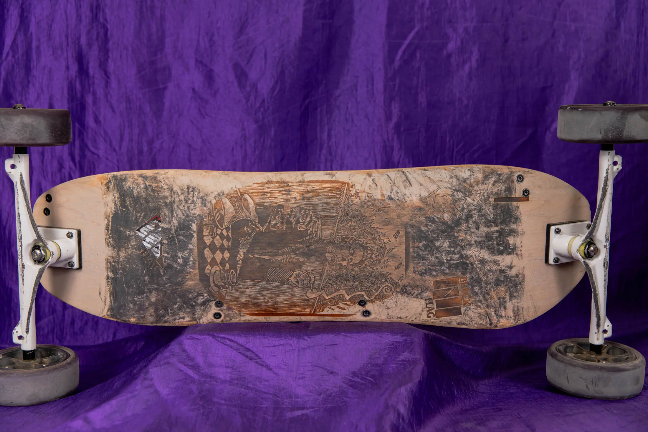 Worn skateboard with purple fabric background.